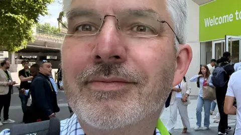 Ian Fogg A close-up selfie of a man with white hair, a white beard and rimless glasses