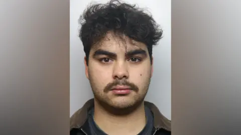 Kyran Smith mugshot. He has dark hair and dark stubble.