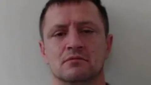 A police mug shot of a man with short dark hair, looking into the camera