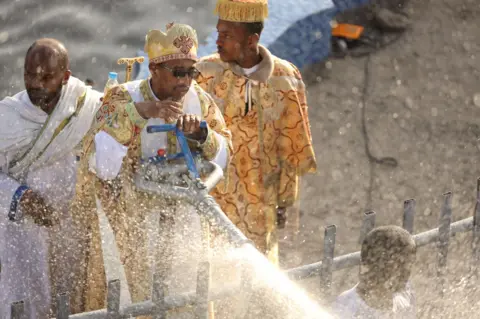 EBC A priest uses a big hose to baptise those people watching on.