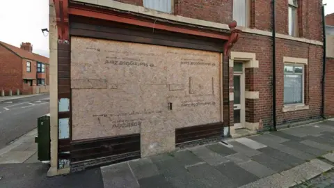 A Google street view screenshot of the takeaway unit on Coomassie Road, Blyth. The unit sits on a street corner and is boarded up. It is set within a residential area.