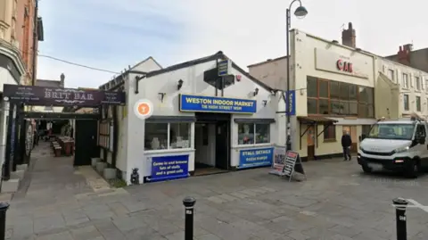 A Google Street View image shows the front of Weston Indoor Market. A single storey building, a blue sign above the door reads "Weston Indoor Market. 116 High Street WSM". 
