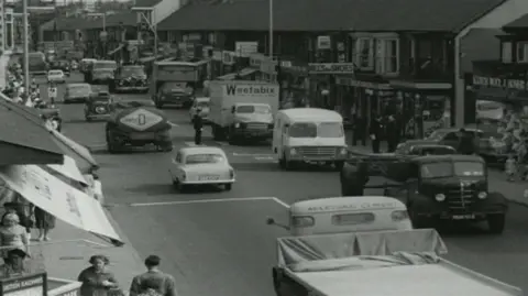 A black and white old image of the old A48 road that runs through Port Talbot from before the M4 motorway was built showing congestion as cars and lorries went slowly through the town