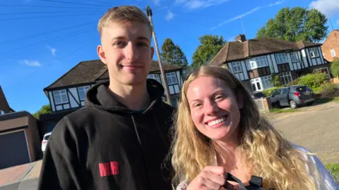 Matthew Hollingham A man and woman are smiling while stood on a residential street on a sunny day