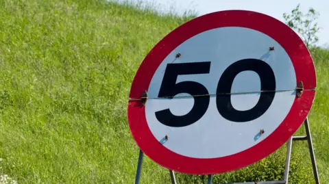 Getty Images A 50mph sign on a stand in front of a green grass banking