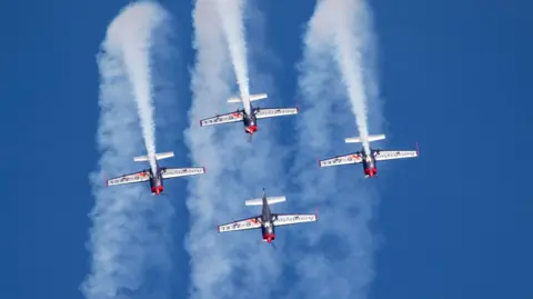 Paul Box Four red, blue and white aircraft during a display amidst blue skies.