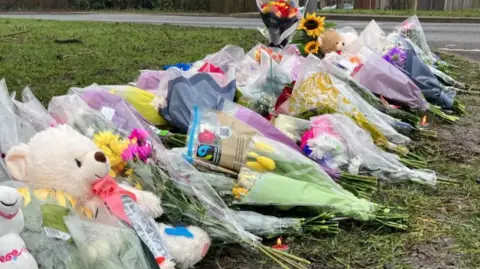 flowers left at the scene of a crash, including a large white teddy bear