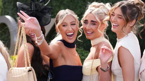PA Media Four women in yellow, black and cream dresses smile and pose for the camera