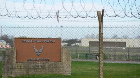 PA Media The entrance of RAF Fairford. There is a brick wall and a brown sign that reads "Royal Air Force Fairford, U.S Air Force, Gate 7. It is behind a large barbed wire fence.