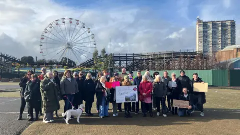 Protesters before the demonstration to save the Scenic Railway at Dreamland, Margate, set off. A number of people, some with signs, can be seen congregated together. The Scenic Railway can be seen in the background.