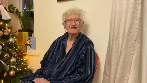 Supplied An elderly man in a dressing gown sits next to a Christmas tree