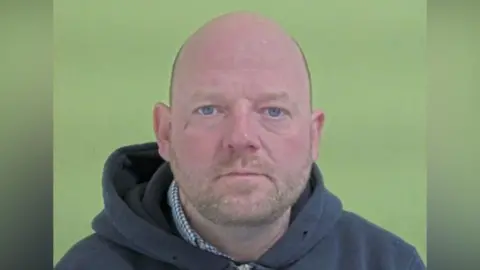 Police mugshot of Ford, who is bald with fair stubble.