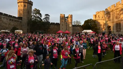 The Myton Hospices Thousands of people stood on the grounds of a castle, wearing pink t shirts, stood behind a barrier