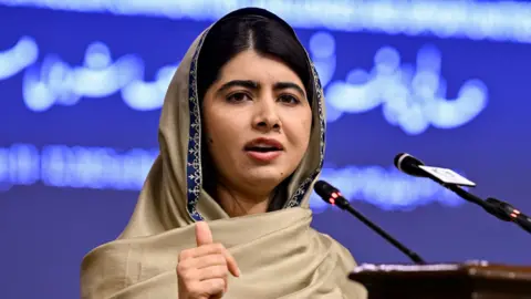 Getty Images Malala speaking at a podium in front of a blue backdrop