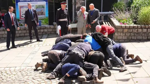 PA Media A scrummage of men on the ground in front of five men standing in suits