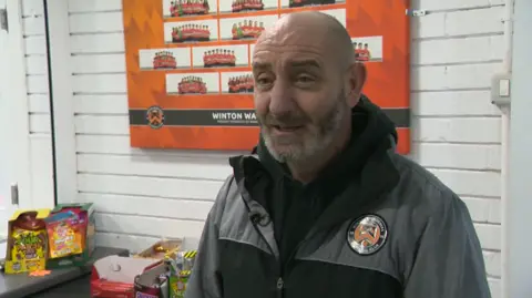 Lee está na sede do clube falando para a câmera.