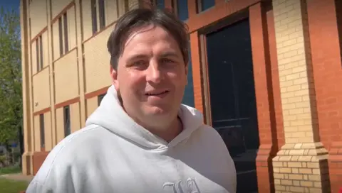 Daniel Jarvis, who has centre-parted dark hair and is wearing a white hoodie, is standing outside South Sefton Magistrates' Court