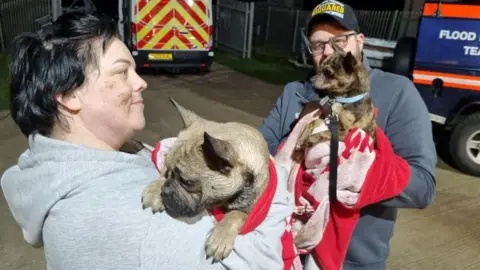 Two people holding the dogs which are wrapped in towels and looking a bit dazed.