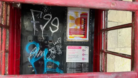 The inside of the phone box - with graffiti where the phone itself used to be. There windows either side of the box.