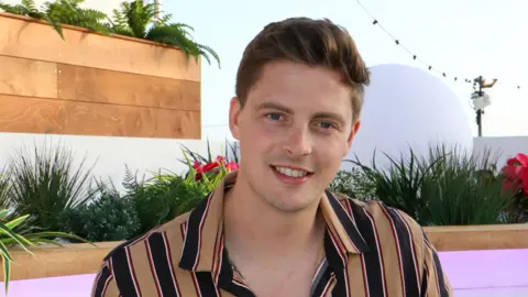 Getty Images Alex George, wearing a brown and blue striped top