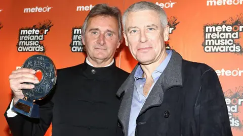 Getty Images DUBLIN, IRELAND - FEBRUARY 19: Lord Henry Mountcharles, who received the Industry Award, poses with U2 band member Adam Clayton at the Meteor Ireland Music Awards at Royal Dublin Society on February 19, 2010 in Dublin, Ireland. (Photo by Phillip Massey/WireImage)
