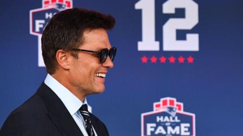 Tom Brady smiles while wearing sunglasses