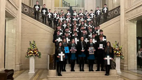 Pupils from St Ciaran’s College standing in the Great Hall at Stormont, holding crosses and images representing the 54 lives killed on the A5 since 2007.