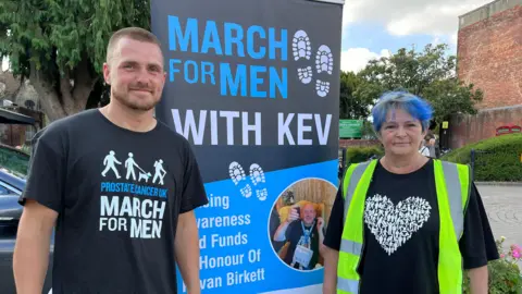 Claire Birkett and a man standing next to a sign which reads "March for Men with Kev"