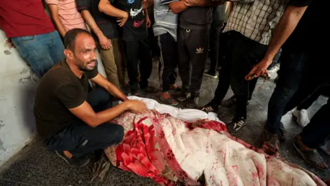 Reuters A Palestinian reacts next to a body, after a school that was sheltering displaced people was hit by an Israeli strike, amid the Israel-Hamas conflict, at a hospital in Gaza City.