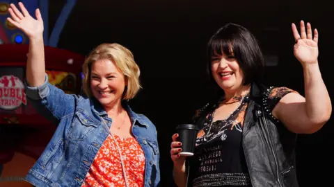 PA Media Joanna Page and Ruth Jones smile and wave to crowds of fans while filming in Barry Island