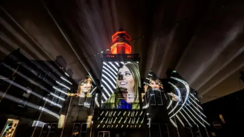 Paul Campbell The projection shows young people smiling. The light also has a stripey effect.