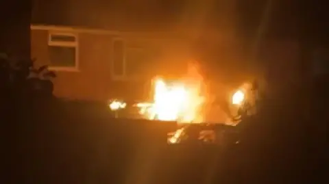 Lisa Smart A picture of a house in the dark with orange flames coming from the ground floor 