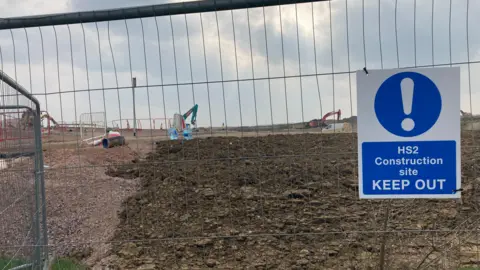 Laura Coffey/BBC A metal fence with a white and blue sign that reads HS2 Construction site Keep Out. Behind the fence there is a number of diggers, a van and more fencing.