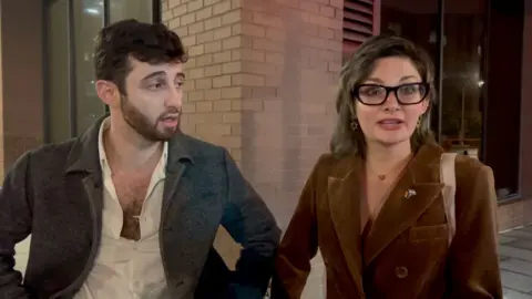 Young man on the left and woman the on right standing on street corner