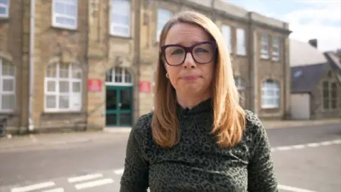 Reporter Nelli bird, who has long light brown hair and glasses and is stood in front of a court building and road. 