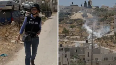Left, a woman in a press vest and helmet walks on a road. Right, smoke rises from a building made of white stone.