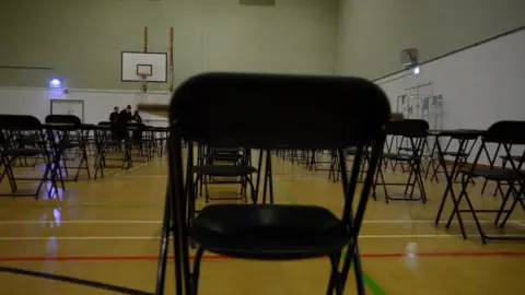 BBC News A sports hall, with tables and chairs acceptable   up   for an exam