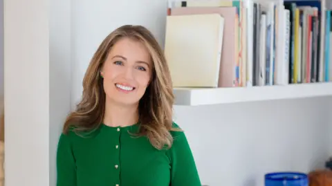 Serena Bolton está rindo da câmera e usando a blusa verde, Federica Amati está ao lado de uma prateleira de livros.