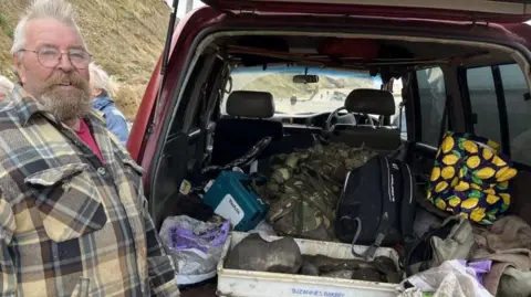 John Clayden with a beard and tartan thermal shirt stands next to an open car boot with the bones in a white plastic tray