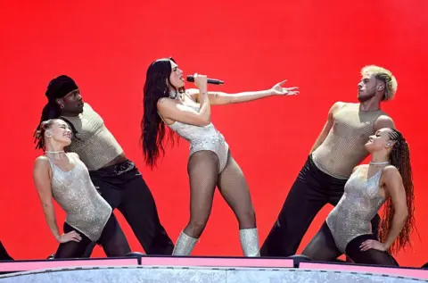 Getty Images Dua Lipa leans back while singing, as dancers frame her on stage