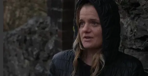 Tiffany Barks is standing in the rain wearing a black anorak with the hood up in the rain