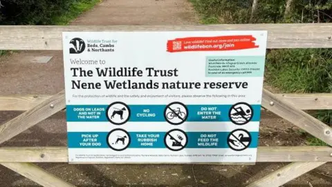 Oliver Conopo/BBC A sign by the Wildlife Trust for Bedfordshire, Cambridgeshire and Northamptonshire which has been put up on a fence at a nature reserve. The sign has rules for visitors including dogs should be kept on leads and not in the water, no cycling and tells people to take their rubbish home.