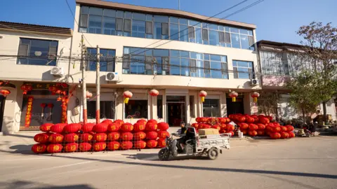 BBC/Benjamin Begley Man riding a small white lorry with red lanterns in the background