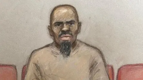 Sketch of Suleiman who looks dead ahead of him and wears a beige jumper. He has a scraggly beard and sits on a row of red seats in front of a blank wall 
