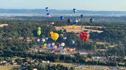 A view over Bristol and the channel with balloons above in different shapes and colours.