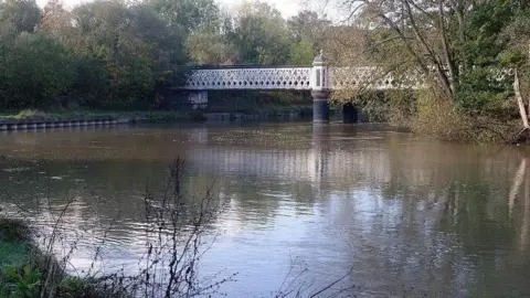 Stephen McKay An iron bridge dating back to the 19th Century spans the Thames, with criss-crossing metal bars forming its sides.