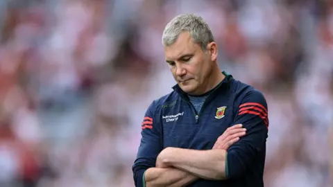 Getty Images A man with short grey hair looks down at his folder arms. He is wearing a navy and red fleece with a Mayo GAA crest.