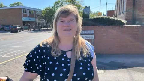 A woman with blonde hair and a black spotty t-shirt on a high street on a sunny day
