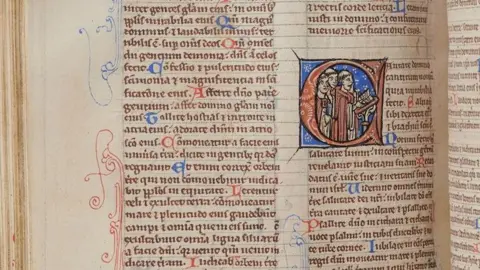 Salisbury Cathedral An old manuscript page, in tiny, perfectly written medieval Latin. One starting letter to a Bible book - a C - is lavishly decorated in blue and red and shows a group of men inside the letter reading from a lectern.