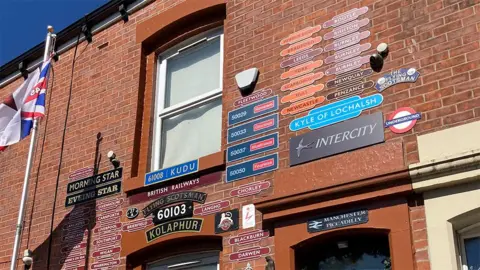 The wall of the red brick terraced house showing the first floor window surrounded by railway signs